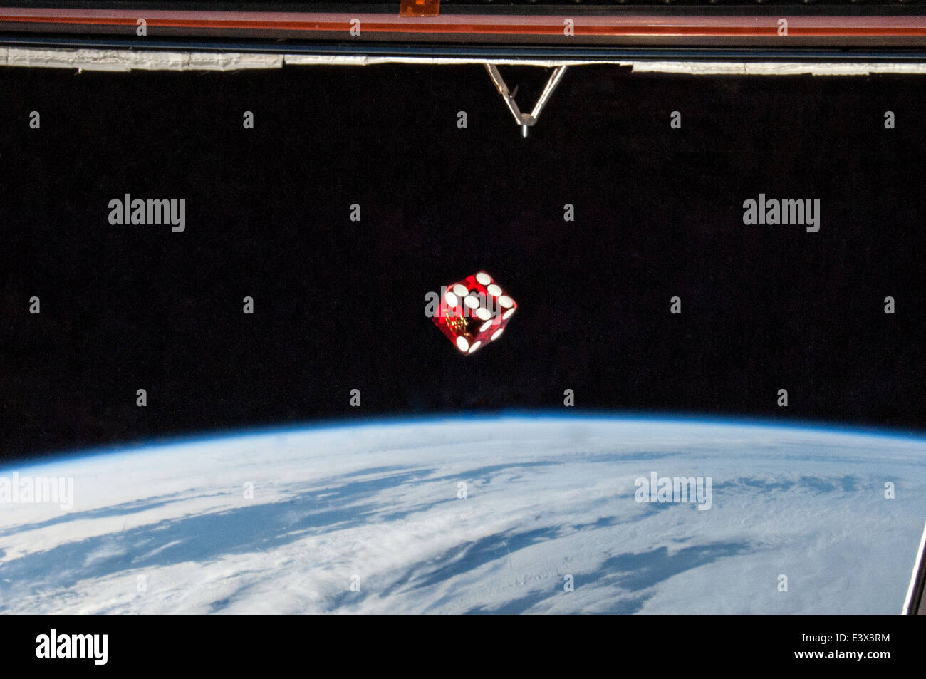 A game dice floats weightlessly inside the International Space Station Cupola with the Earth in the background May 31, 2014 in Earth Orbit. Stock Photo