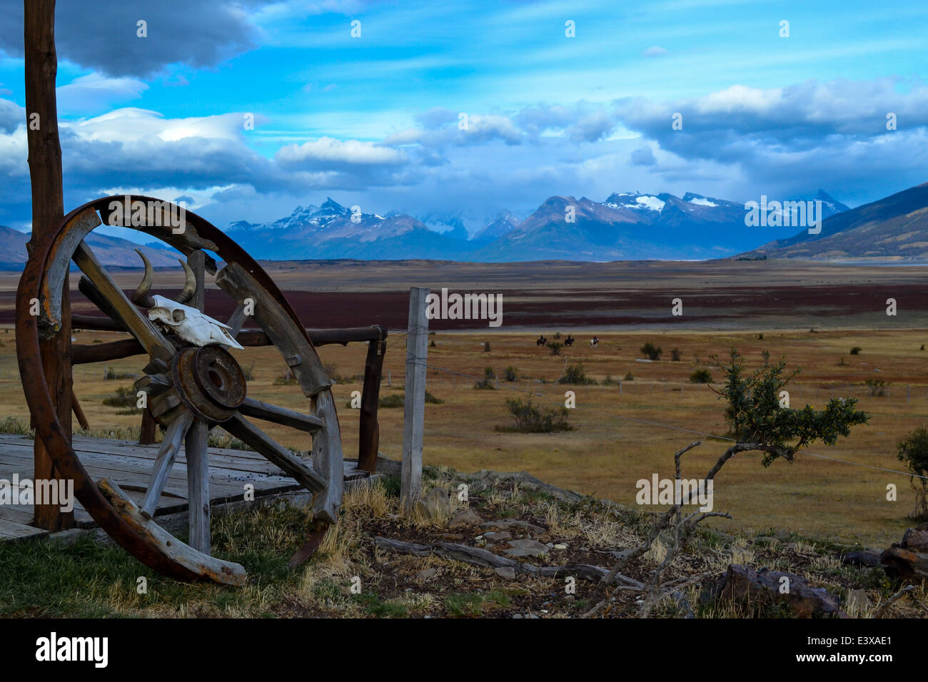Plains of Argentinian Patagonia with glacier-topped mountains in the background and an old wagon wheel resting against a post. Stock Photo
