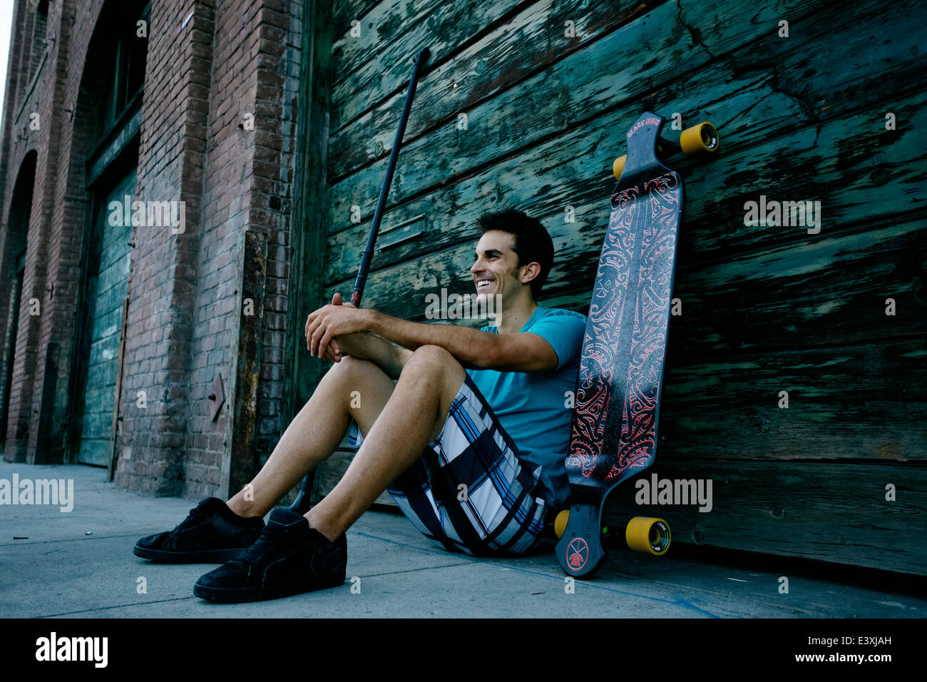 Caucasian man sitting with skateboard and land paddle Stock Photo