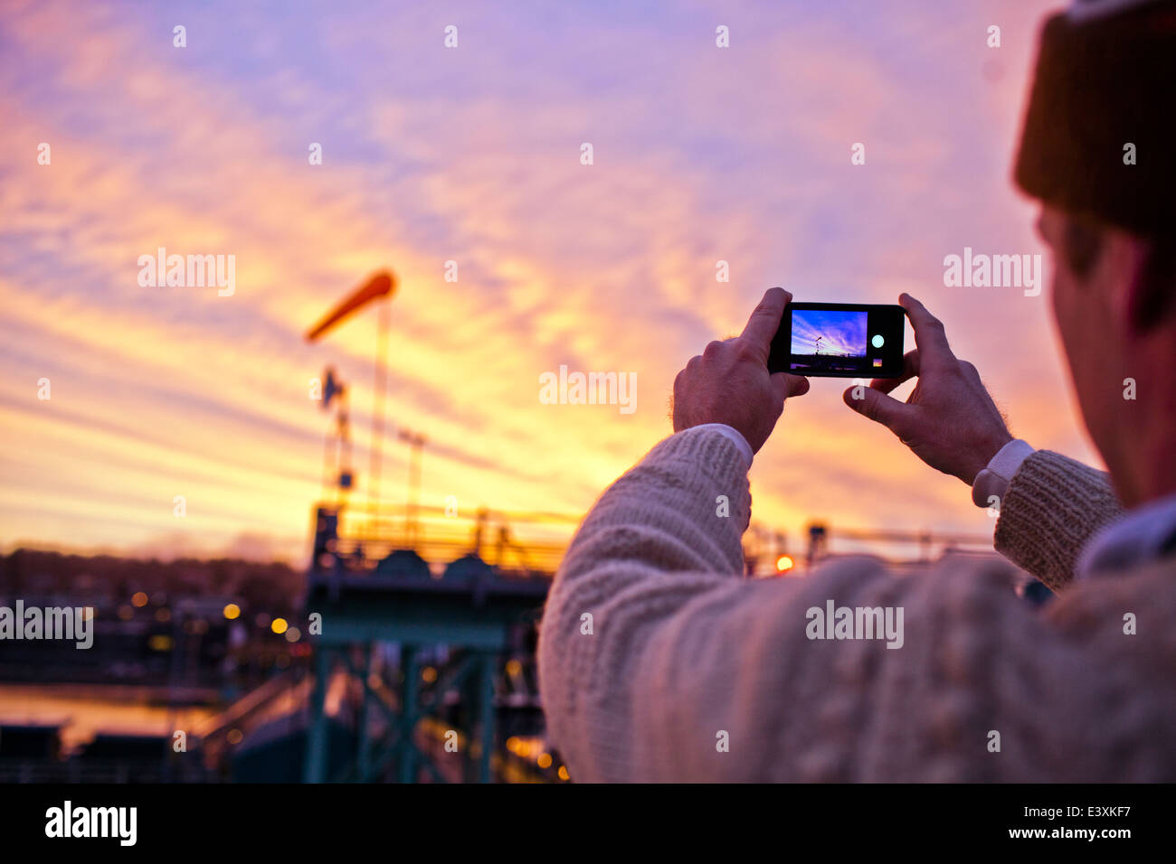 Man taking picture of sunset over bridge Stock Photo