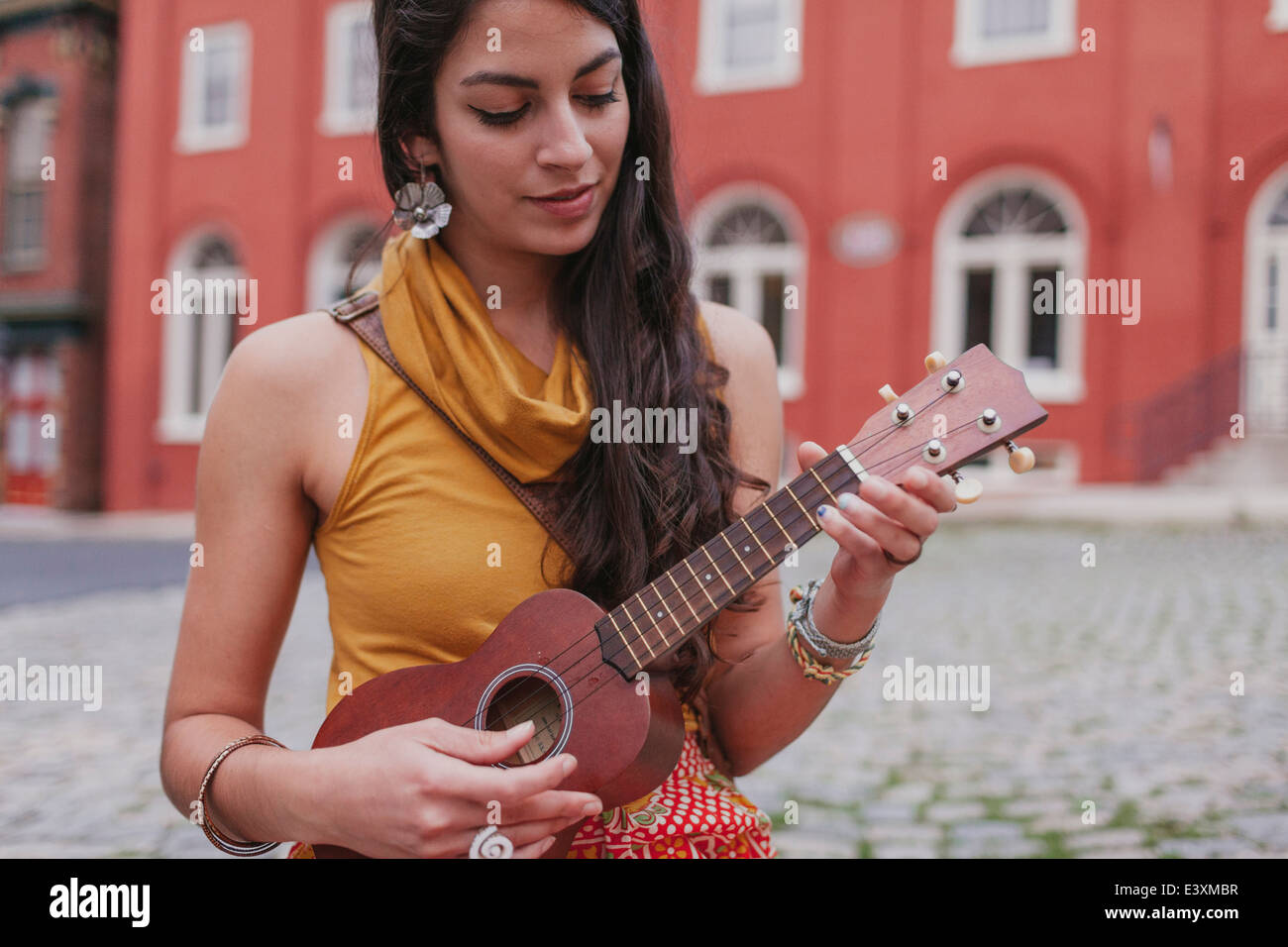 Mixed race woman playing ukulele on city street Stock Photo