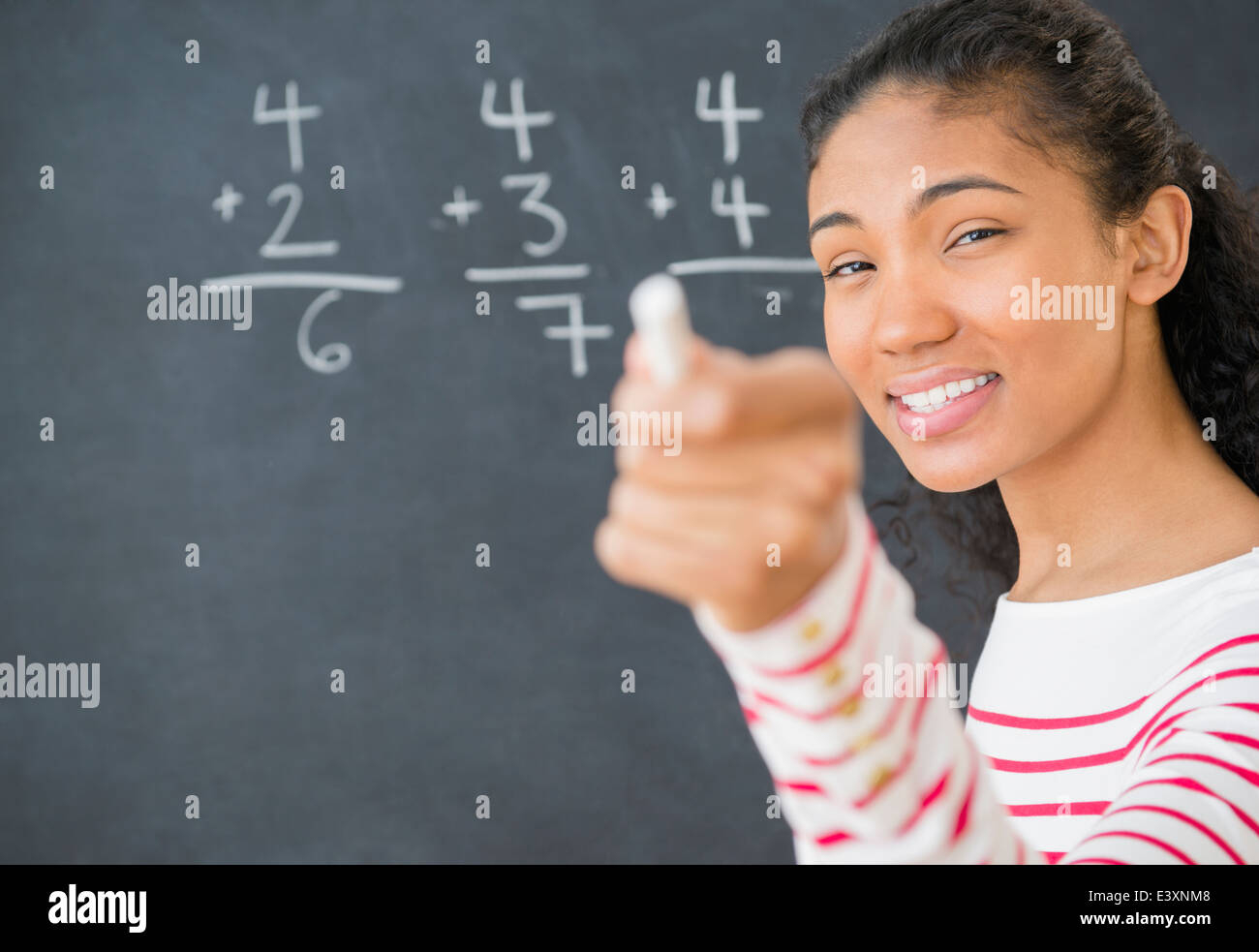 Mixed race teacher doing math on chalkboard Stock Photo