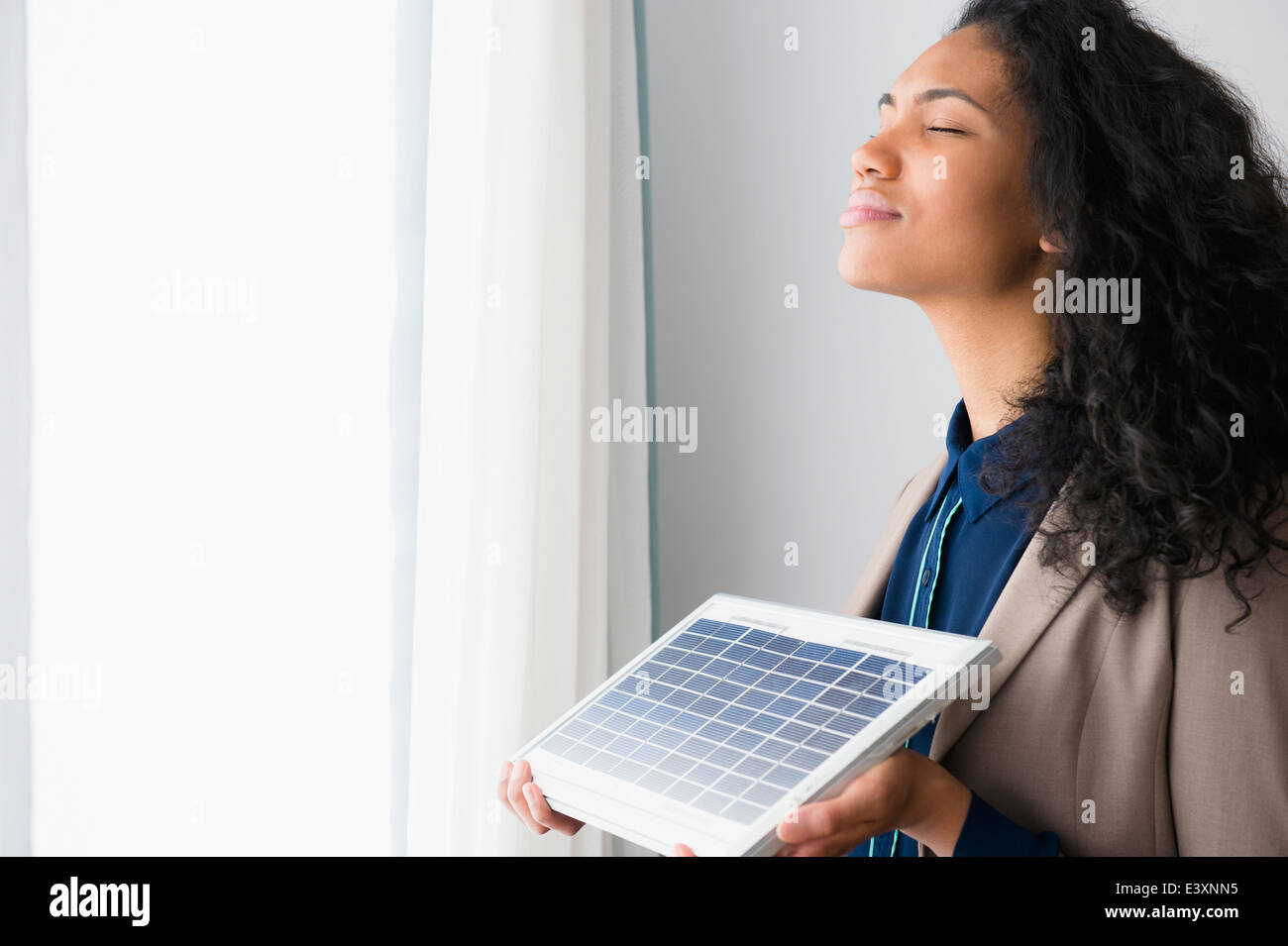Mixed race woman holding solar panel by window Stock Photo