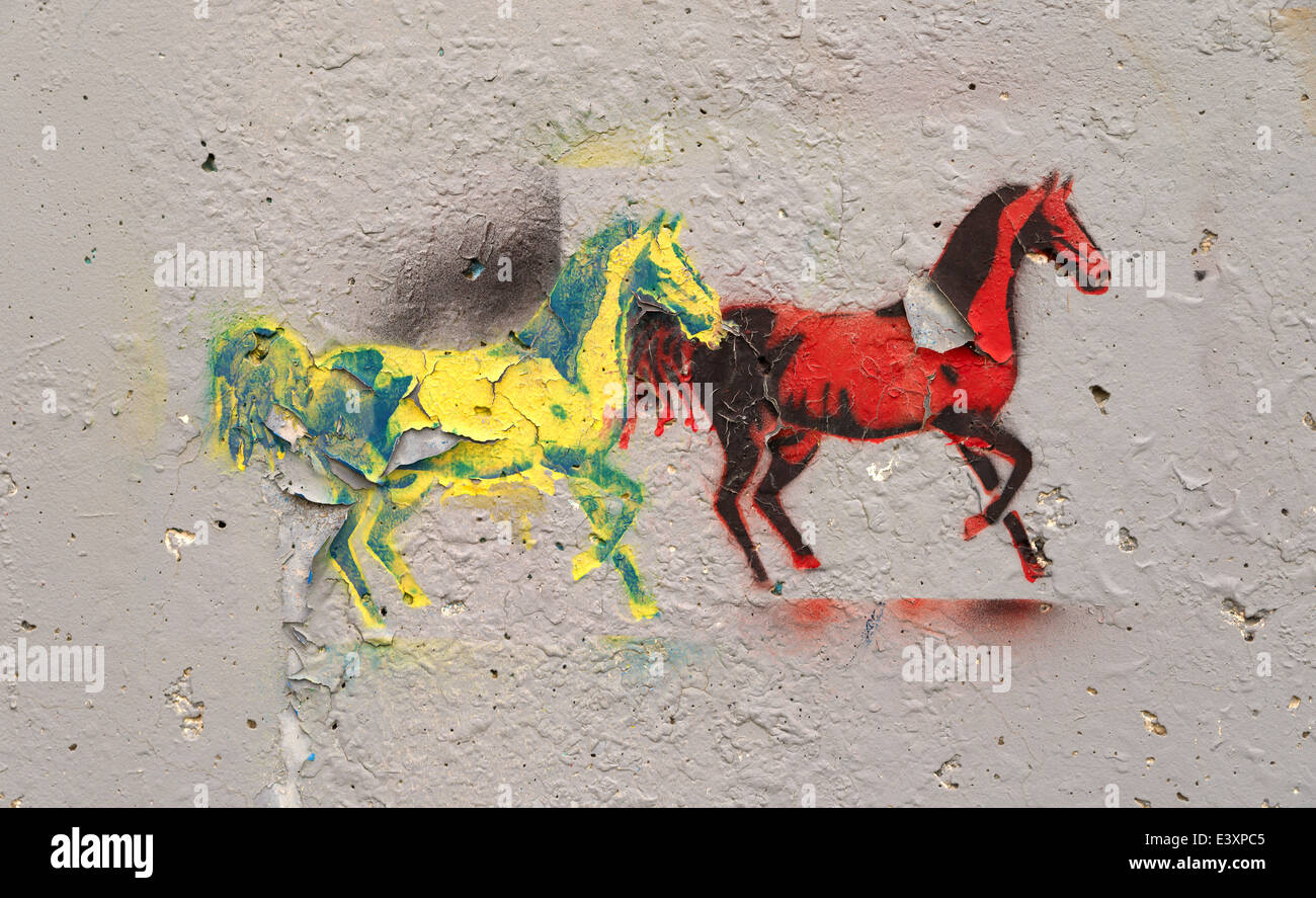 A peeling graffiti image of two horses in bright paint on a concrete wall. Stock Photo