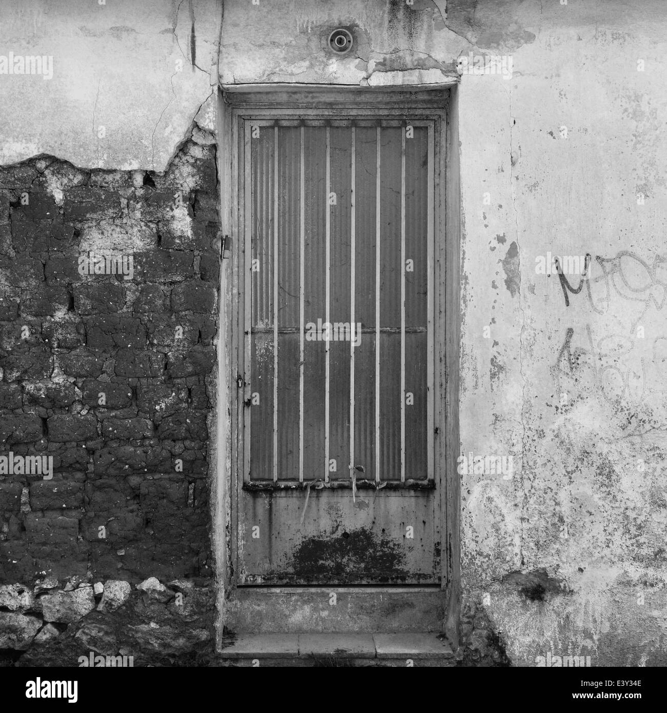 Rusty door and textured broken wall abandoned house exterior. Black and white. Stock Photo