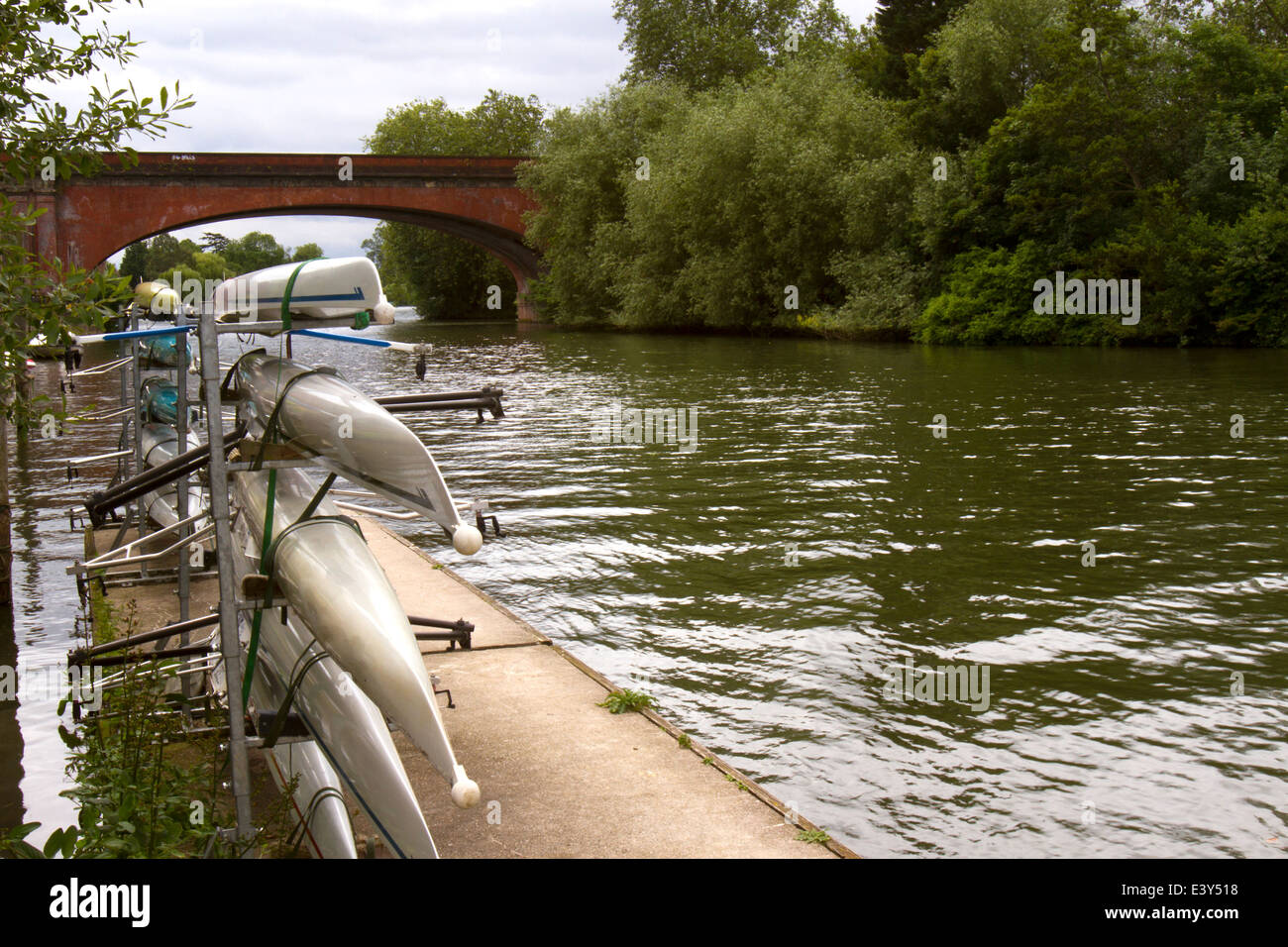 Canoes stacked on a rack next to the river Thames with historic brick railroad bridge in background Stock Photo