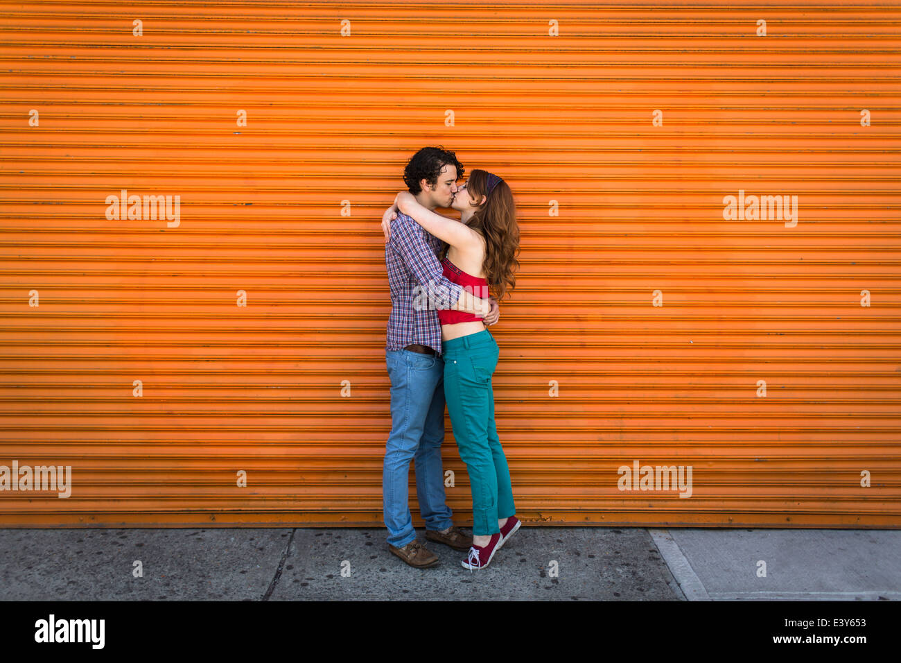 Romantic couple kissing in front of orange shutter Stock Photo