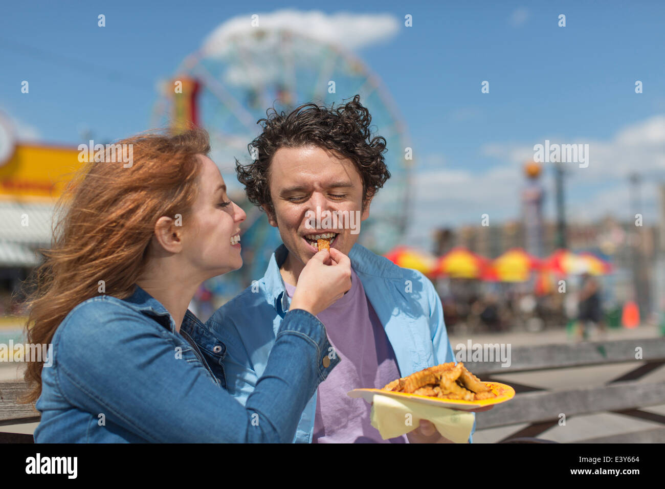 Romantic couple feeding each other chips at amusement park Stock Photo