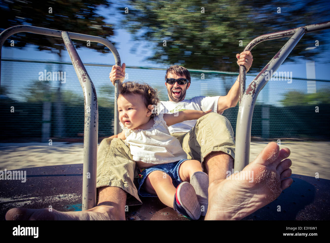 Father and toddler daughter spinning on park roundabout Stock Photo