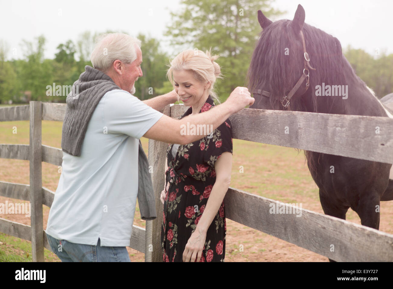 Horse watching mature couple over fence Stock Photo