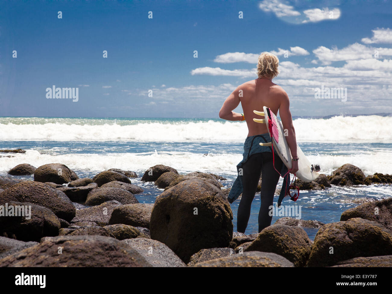 Young adult male surfer watching sea from beach rocks Stock Photo