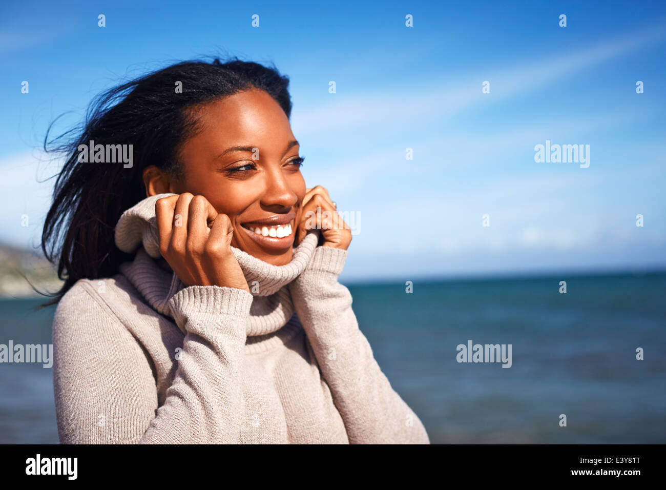 Portrait of young woman holding rollneck on sweater at beach, Malibu, California, USA Stock Photo