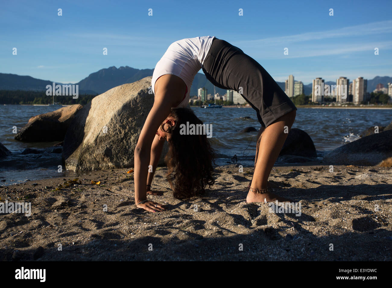 Young Indian woman doing a bridge stretch on the beach in Vancouver, Canada. Stock Photo