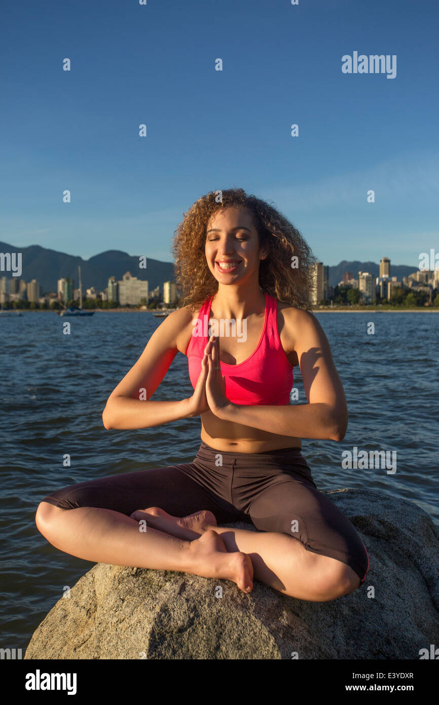 Smiling girl meditating on a rock with the ocean as a backdrop in Vancouver, Canada. Stock Photo