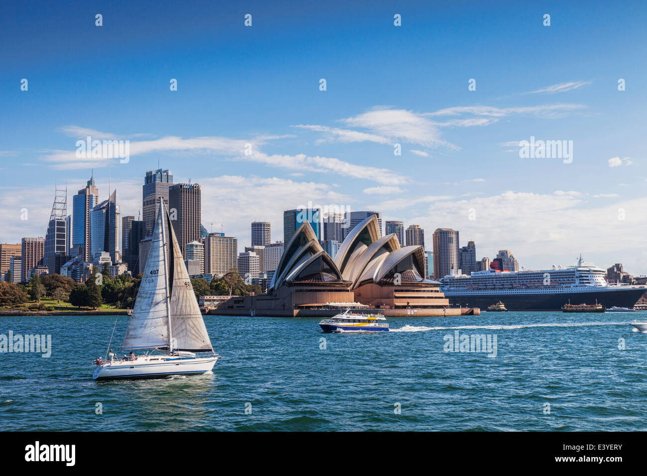 Sydney Harbour, Australia, with Sydney Opera House, a sailing boat, the CBD and Queen Mary 2 moored in Circular Quay. Stock Photo