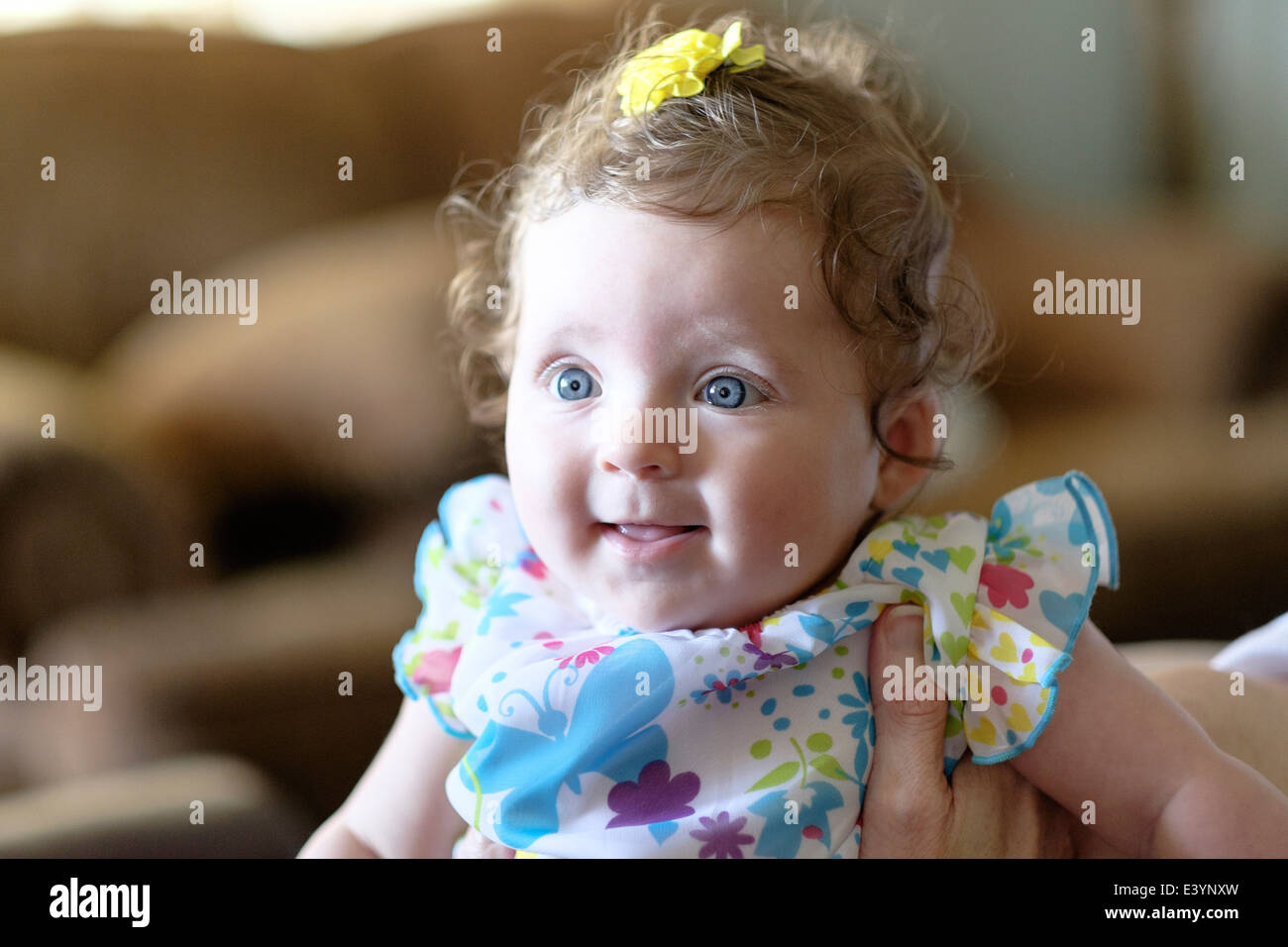 A three month old Caucasian infant girl being held by an adult and smiling. Stock Photo