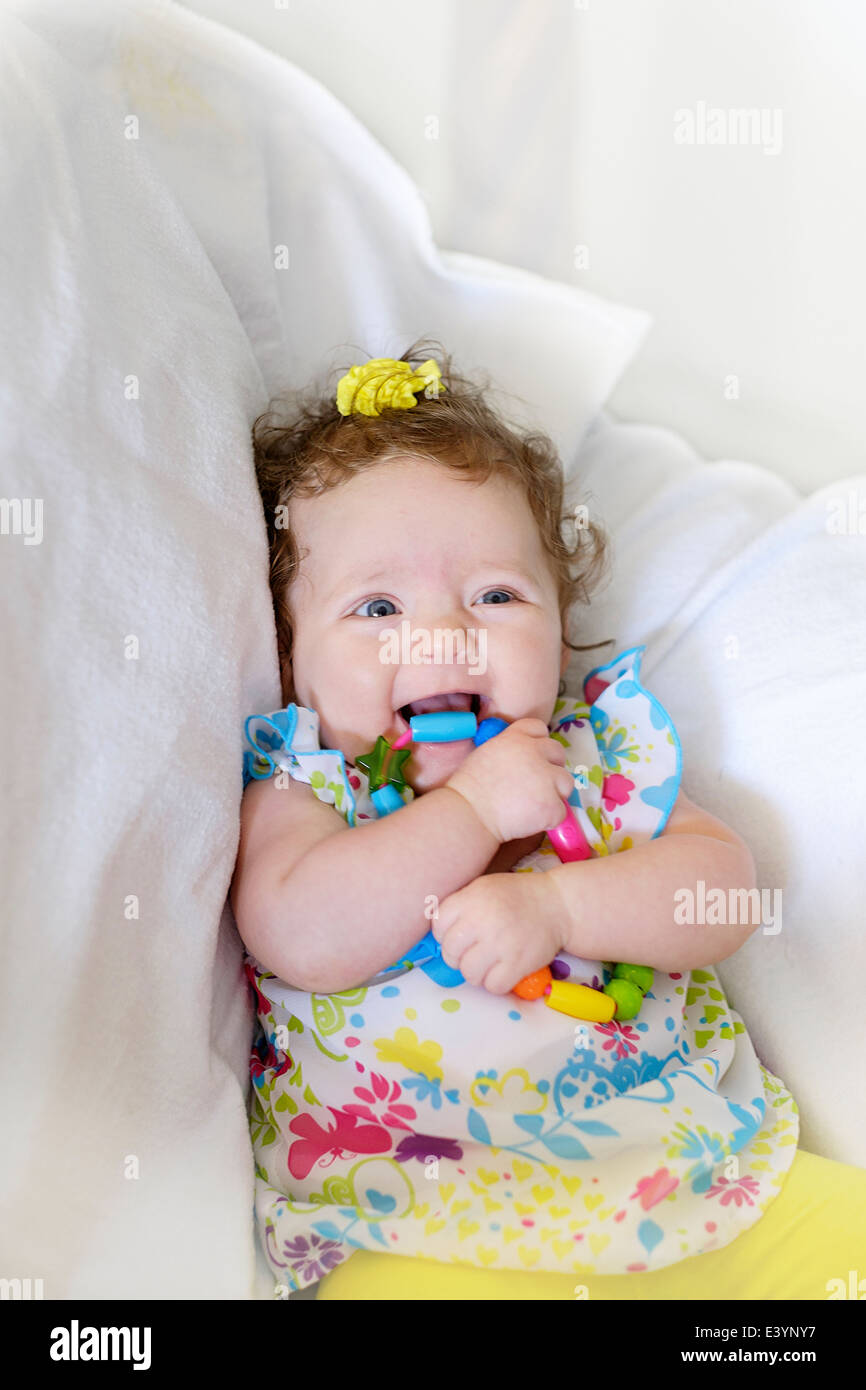 A three month old Caucasian infant girl, smiling while chewing on a teething toy. Sitting up. Background digitally changed. USA Stock Photo
