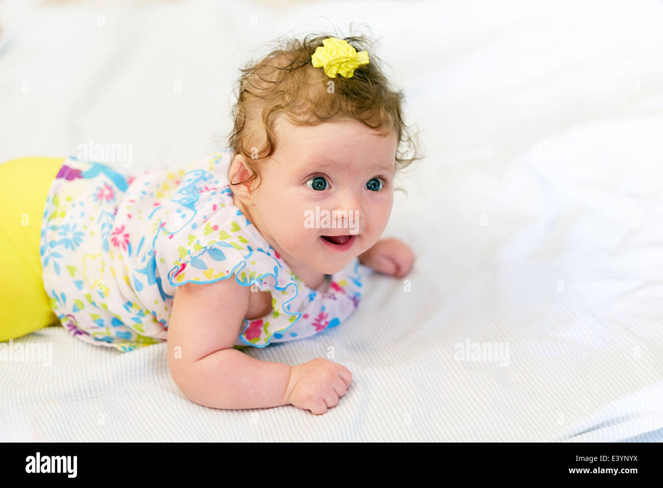 A three month old Caucasian infant girl lying on her stomach and smiling. Yellow clothing and white blanket. Closeup. Stock Photo