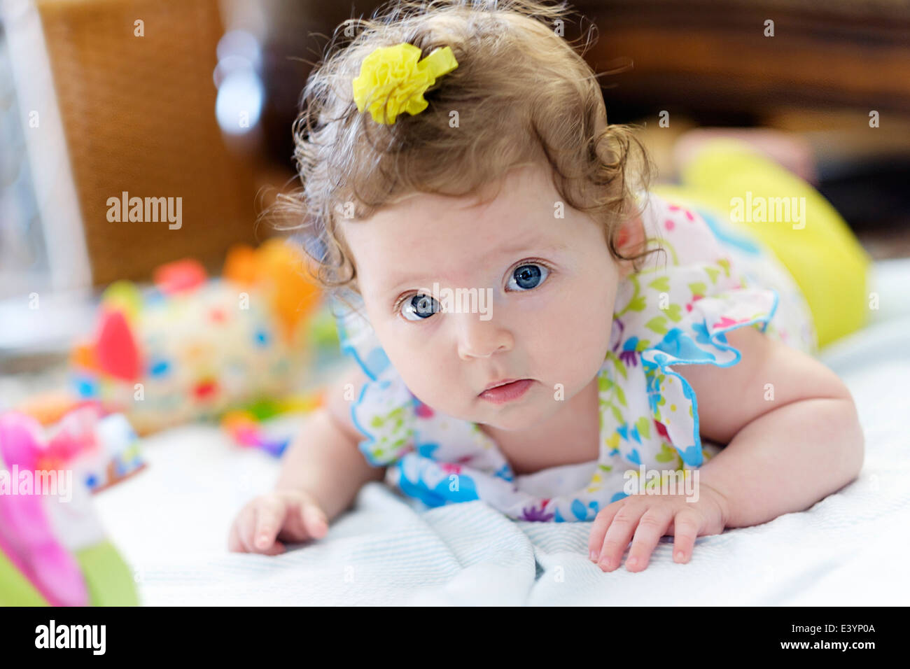 A three month old Caucasian infant lying on her stomach surrounded by toys. Stock Photo
