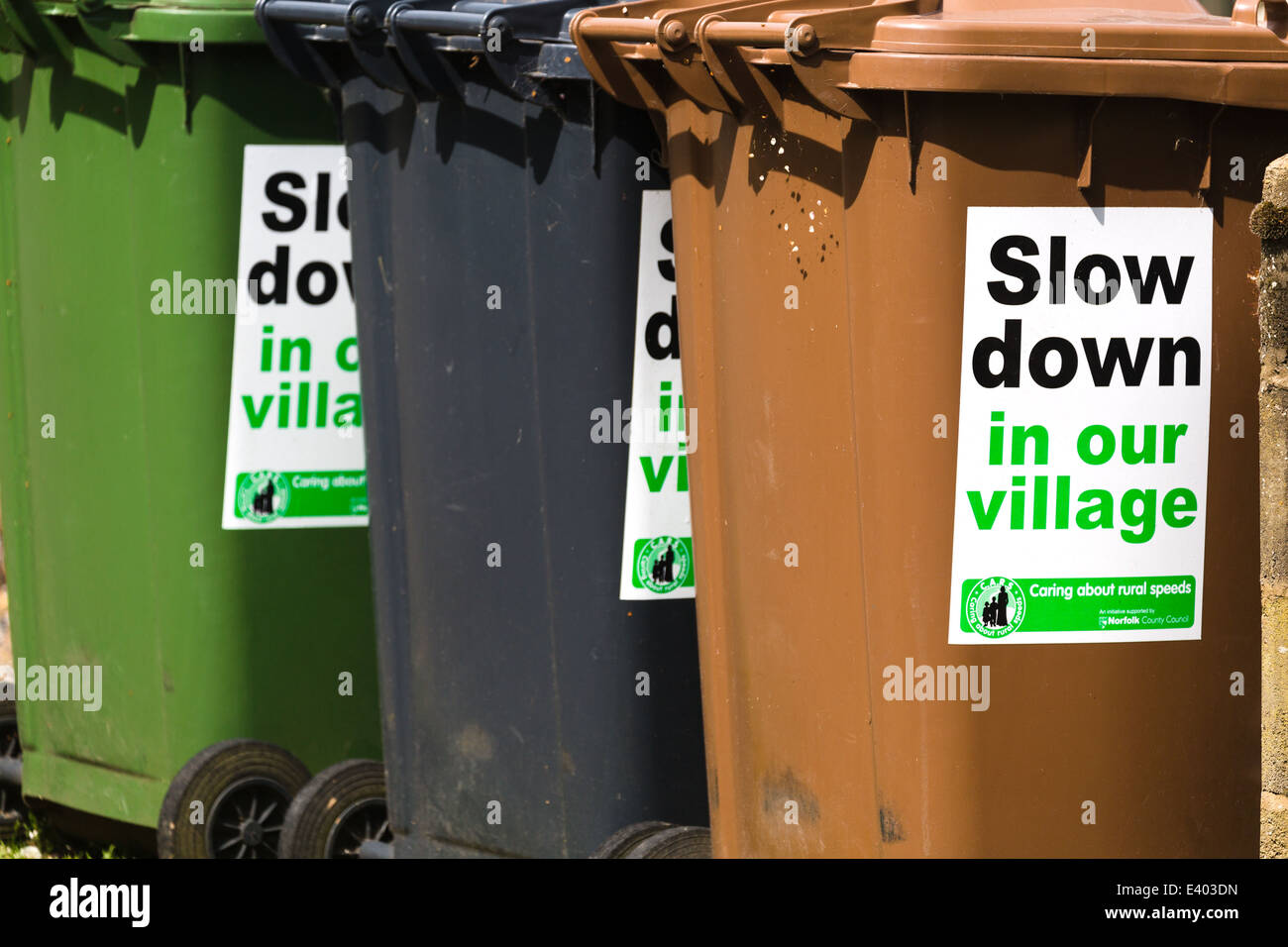 'Slow Down in our Village'; signs attached to local council re-cycling bins. Norfolk. UK Stock Photo