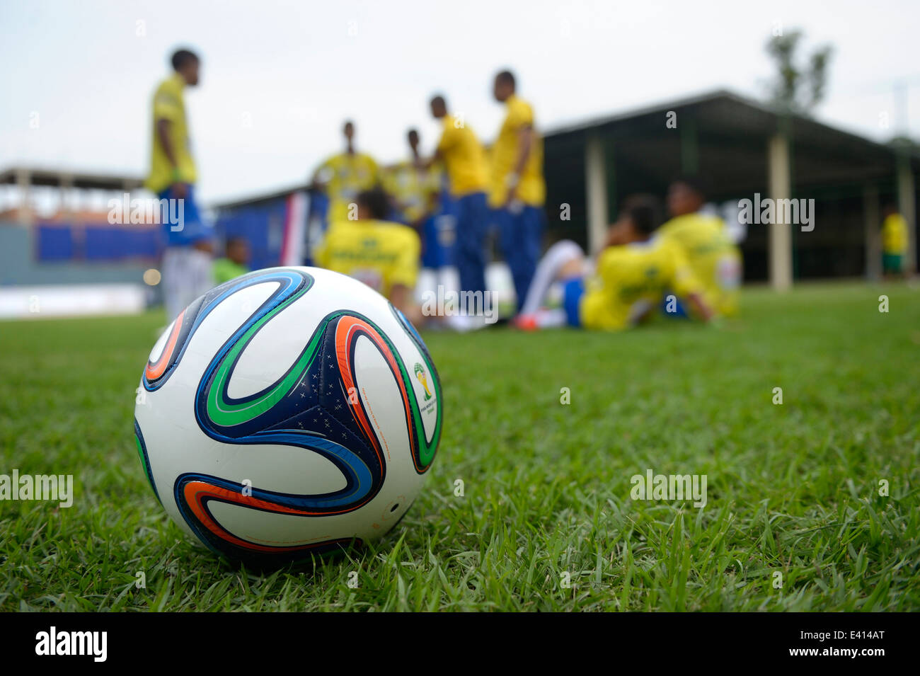 Brazil, Rio de Janeiro, Brazuca lying on meadow, in the background football team of Street Child World Cup 2014 Stock Photo