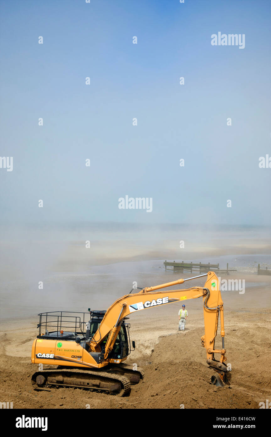 Excavator digging out sand on beach in sea mist Stock Photo Alamy