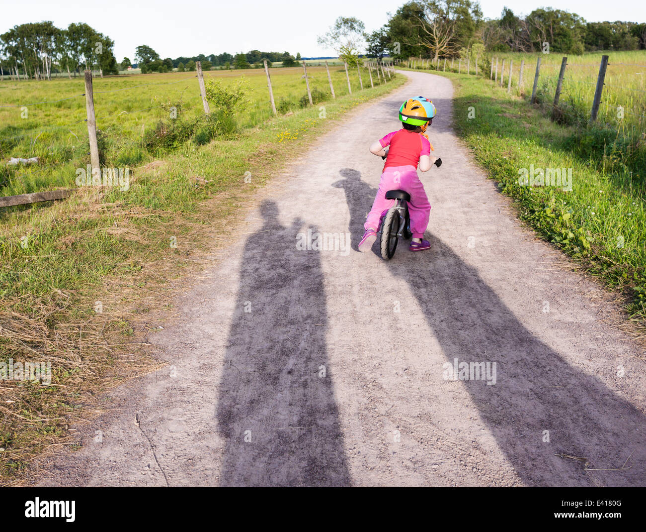 Tranquil summer landscape. Little girl riding a bike on a rural road in Sweden. Stock Photo