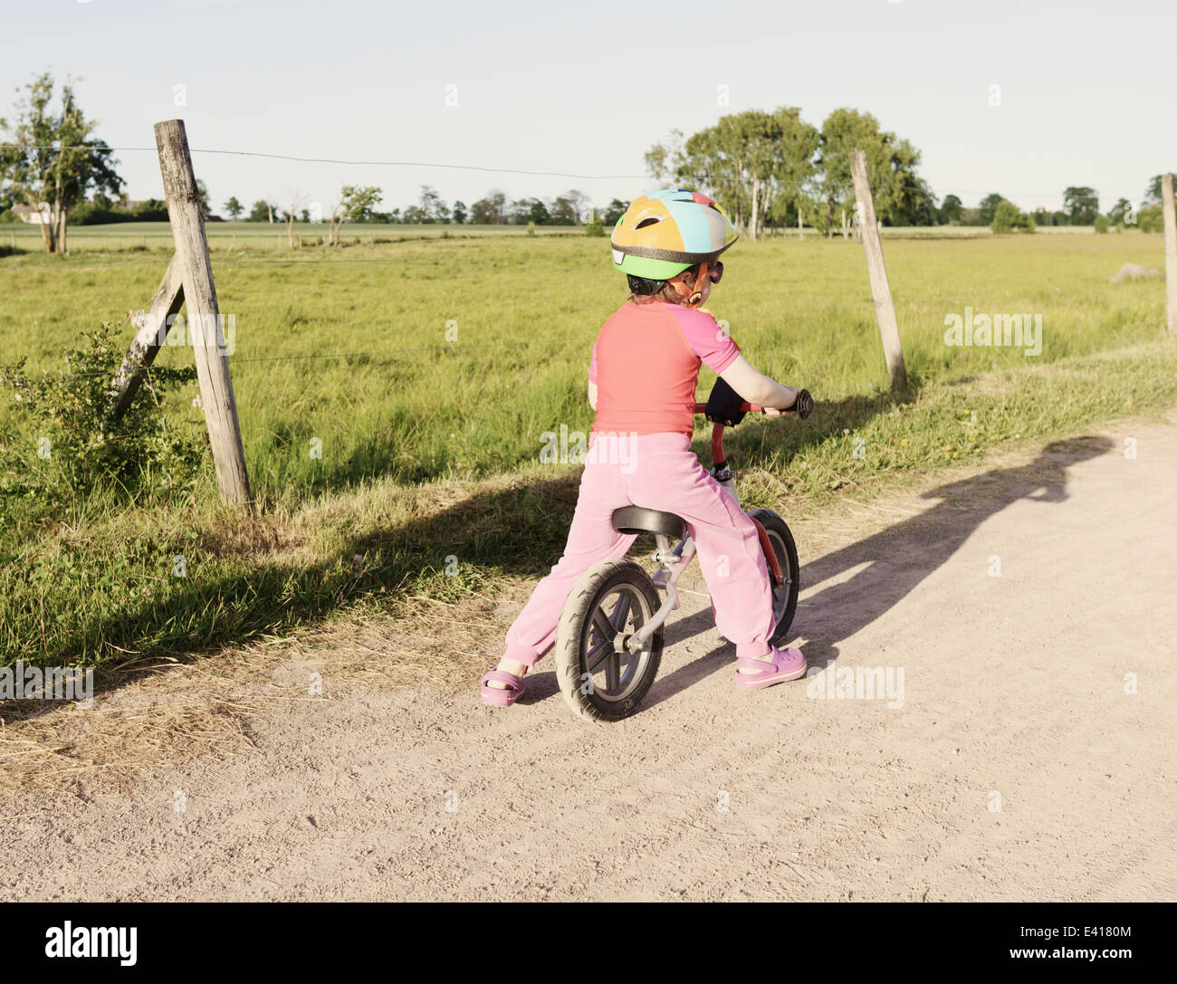 Tranquil summer landscape. Little girl riding a bike on a rural road in Sweden. Stock Photo