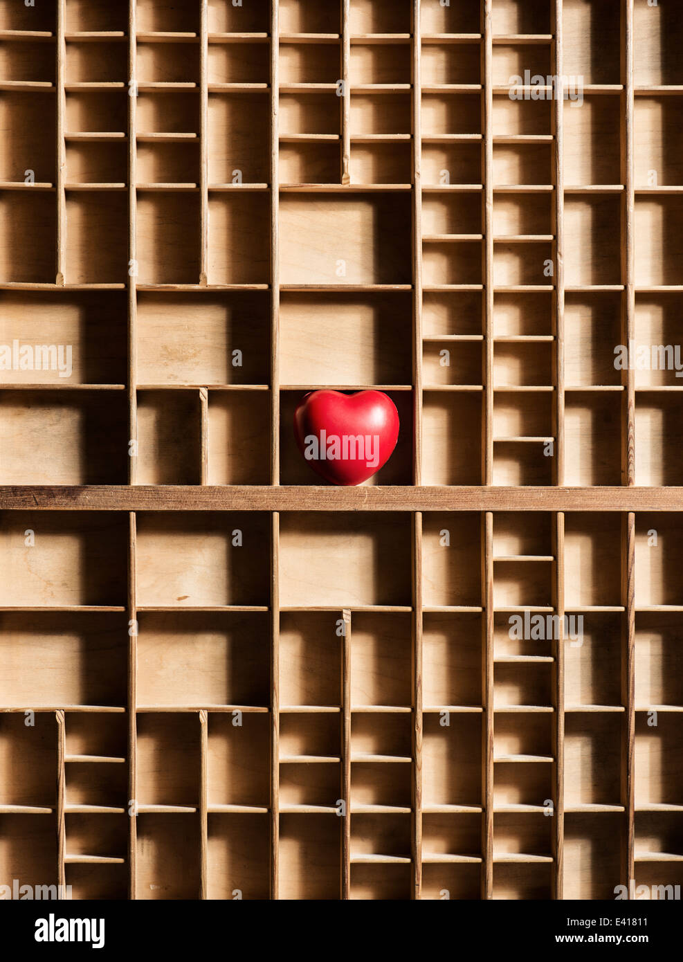 Red heart in empty wooden box with many compartments. Conceptual image of lost love, loneliness and hidden romantic feelings. Stock Photo