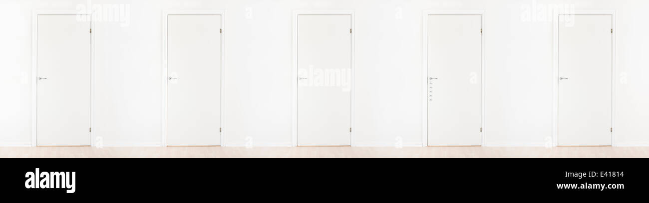 White doors in a row. One door has many locks, the others lack a lock. Conceptual image of security, privacy and safety. Stock Photo