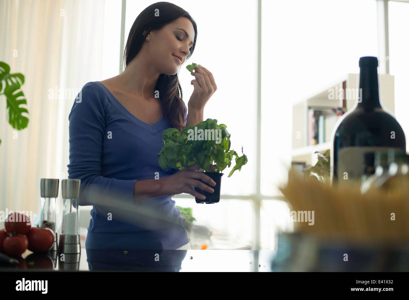 Young woman smelling basil plant in kitchen Stock Photo Alamy