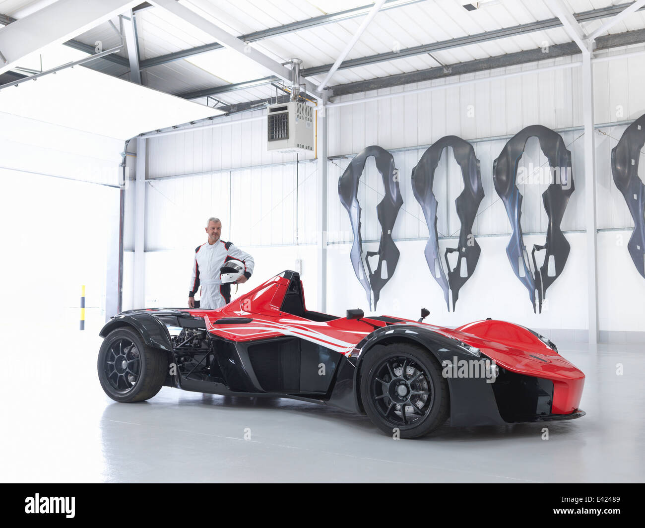 Racing driver with supercar in factory with carbon fibre car body shells on wall Stock Photo