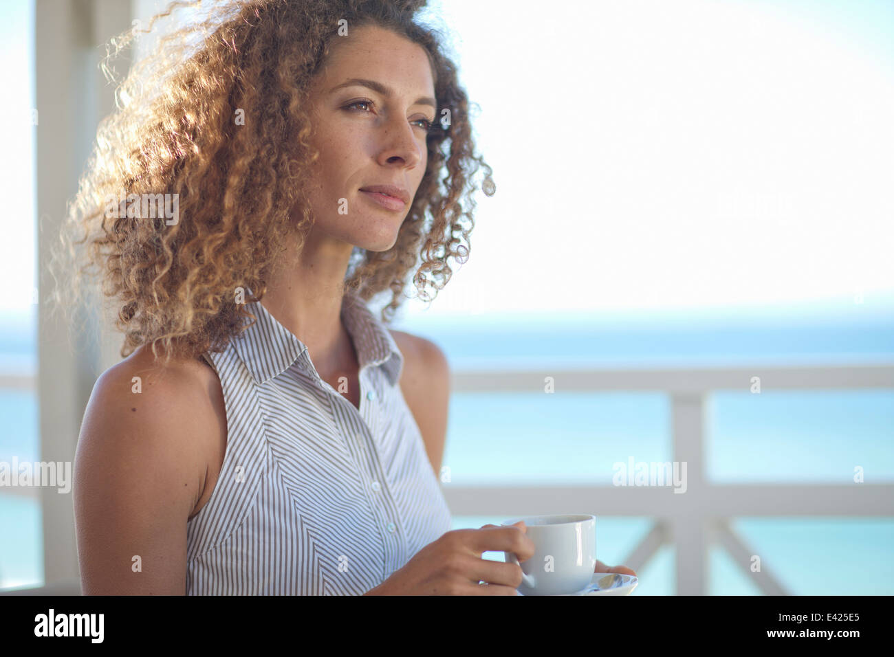 Young woman gazing out to sea from beach house balcony Stock Photo