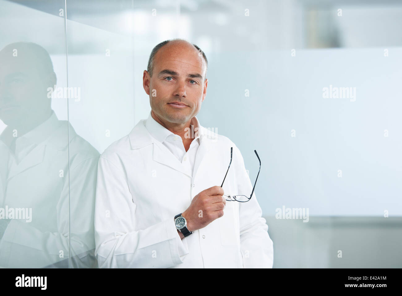 Male doctor leaning against reflective wall Stock Photo