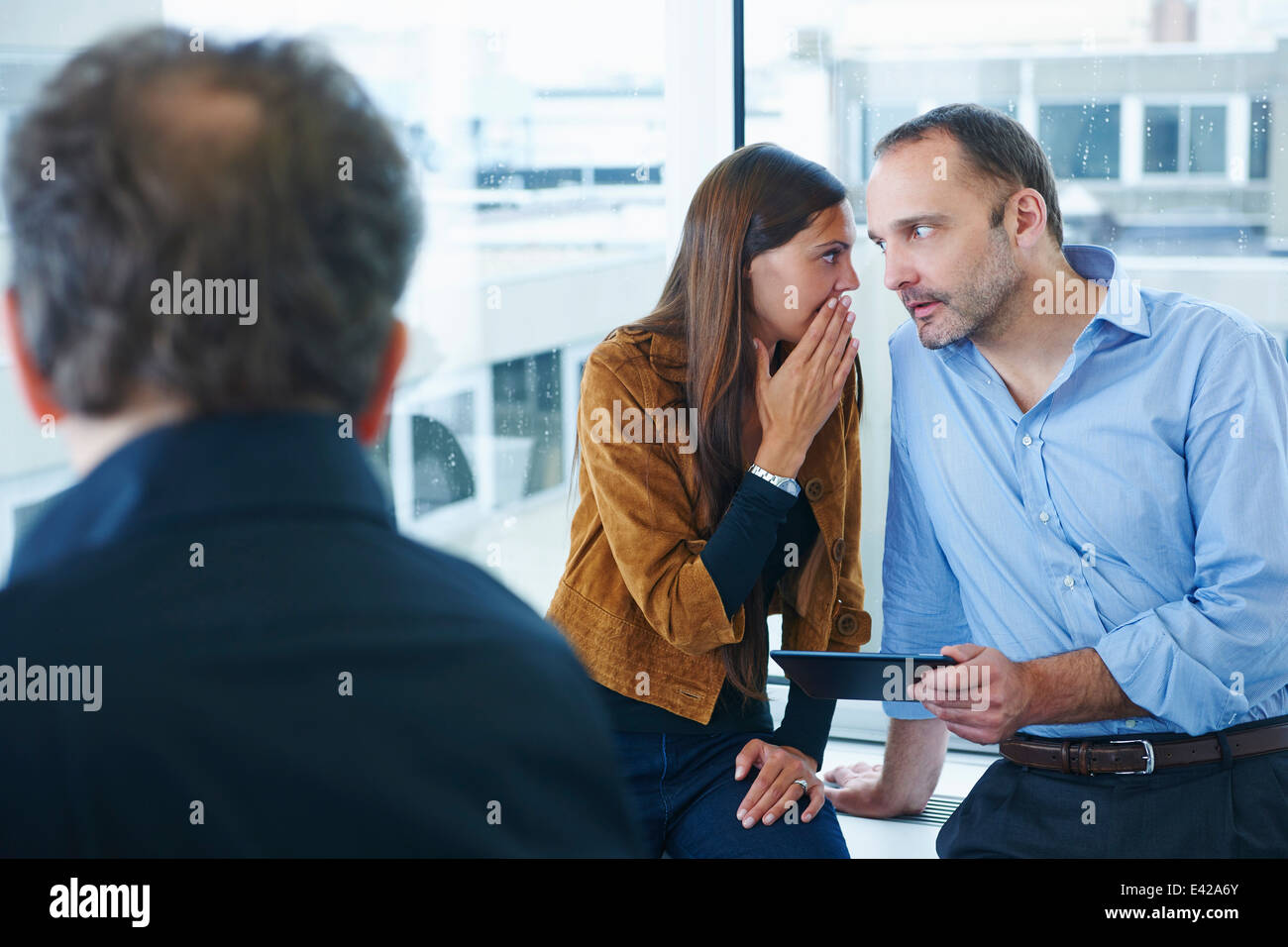 Businesswoman whispering to man in office Stock Photo
