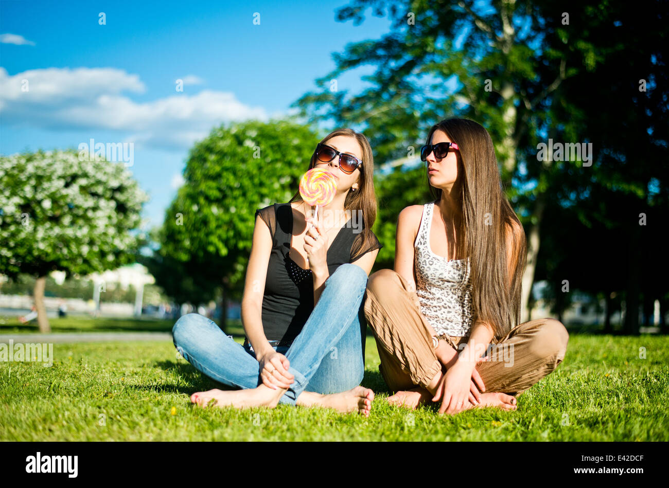 Two young female friends in park, one licking lollipop Stock Photo