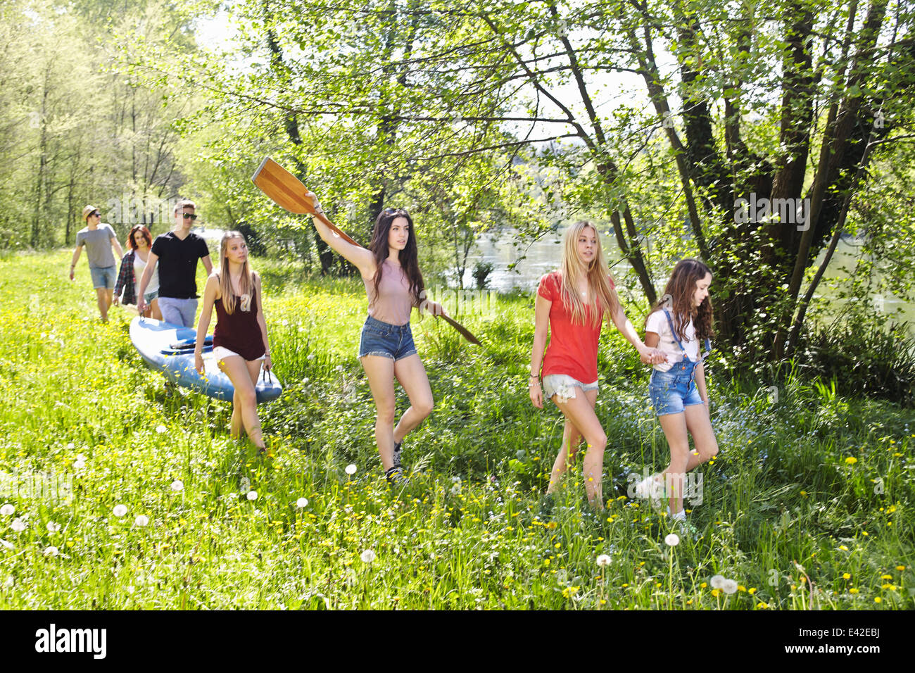 Group of friends walking through grass carrying canoe Stock Photo