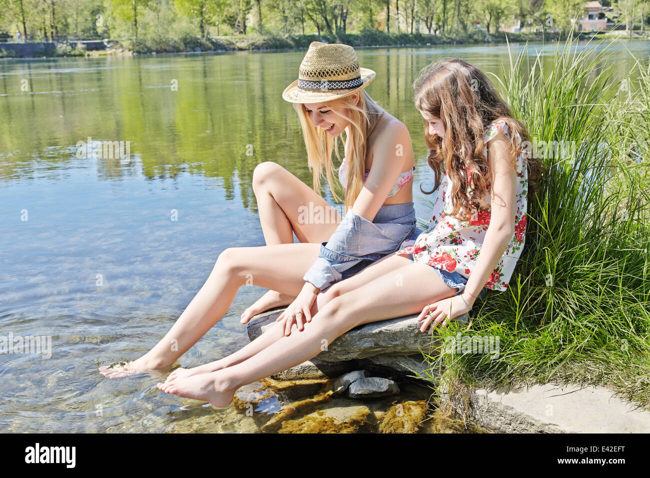 Two friends sitting on rocks by water Stock Photo