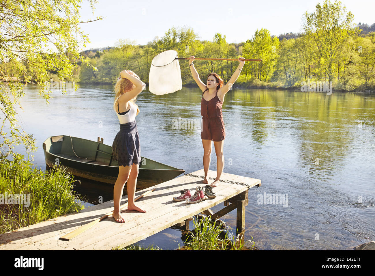 Young women standing on jetty, one holding fishing net Stock Photo