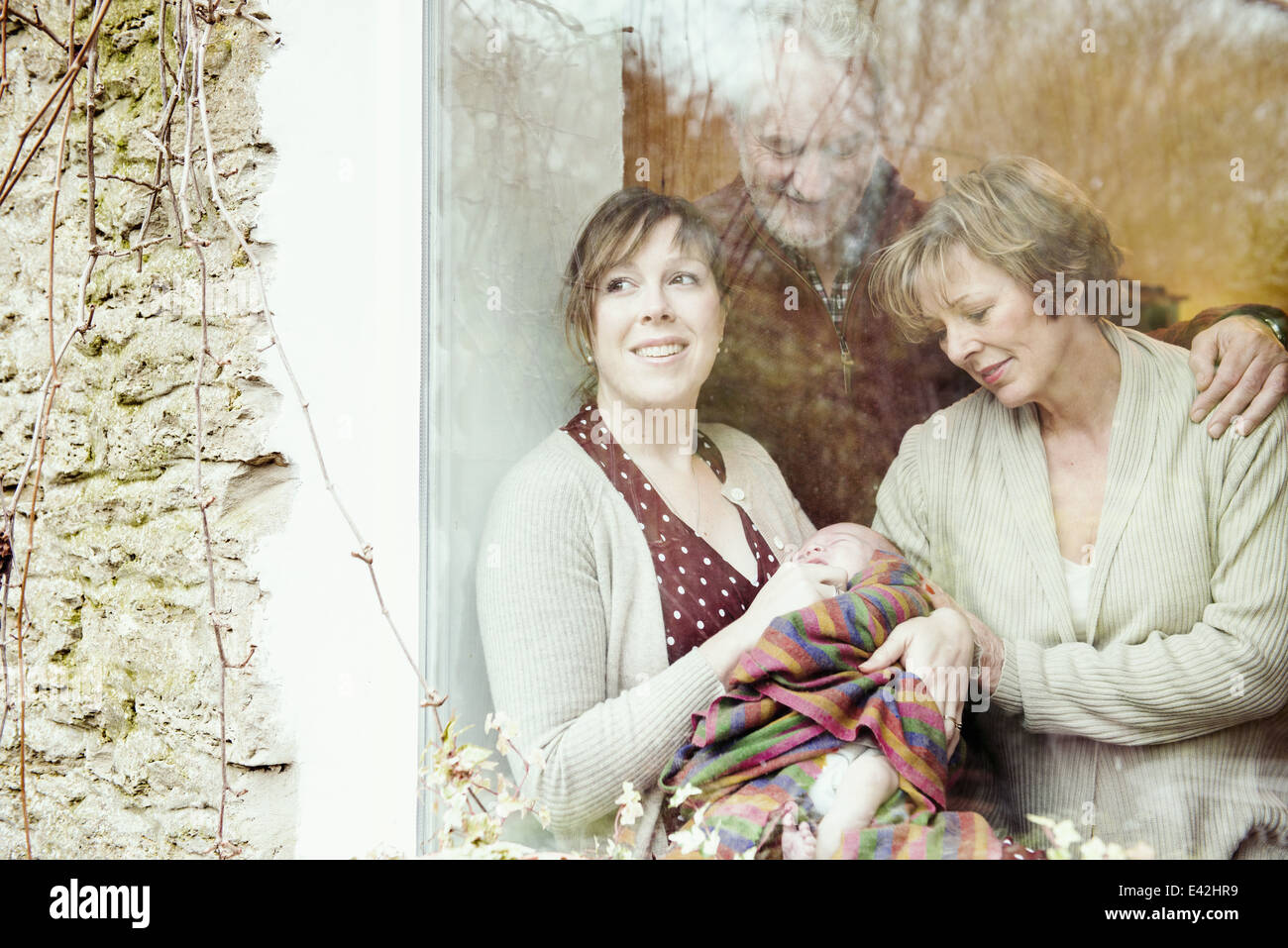 Mother with baby and grandparents looking out of window Stock Photo