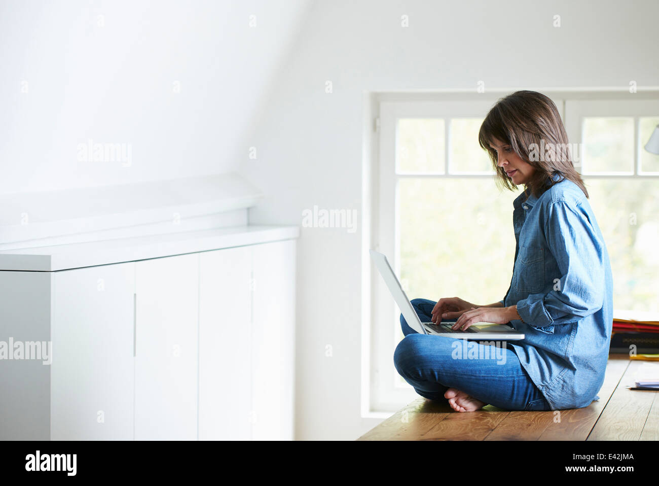 Businesswoman sitting on desk, legs crossed, using laptop Stock Photo