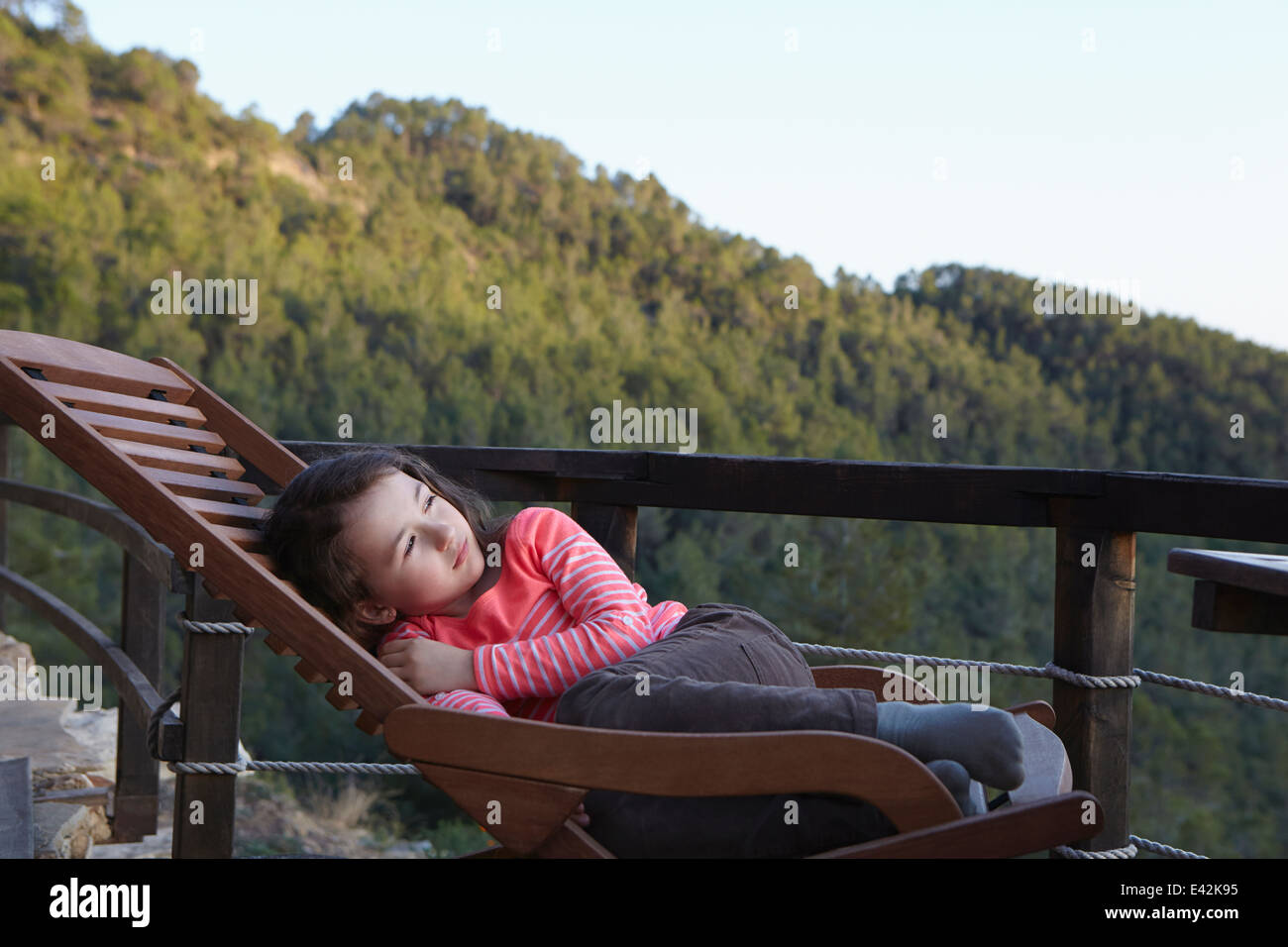 Young girl curled up on balcony deckchair gazing upward Stock Photo
