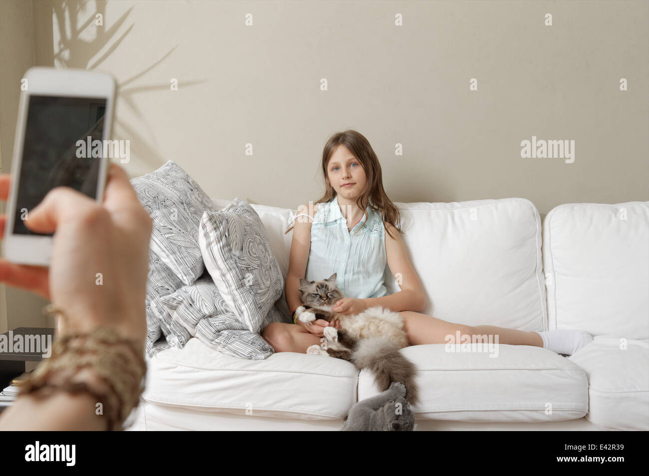 Mother photographing daughter with cat on sofa Stock Photo