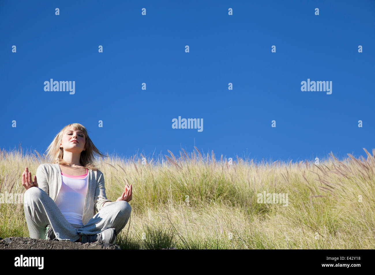 Young woman in yoga position on grassy hill Stock Photo