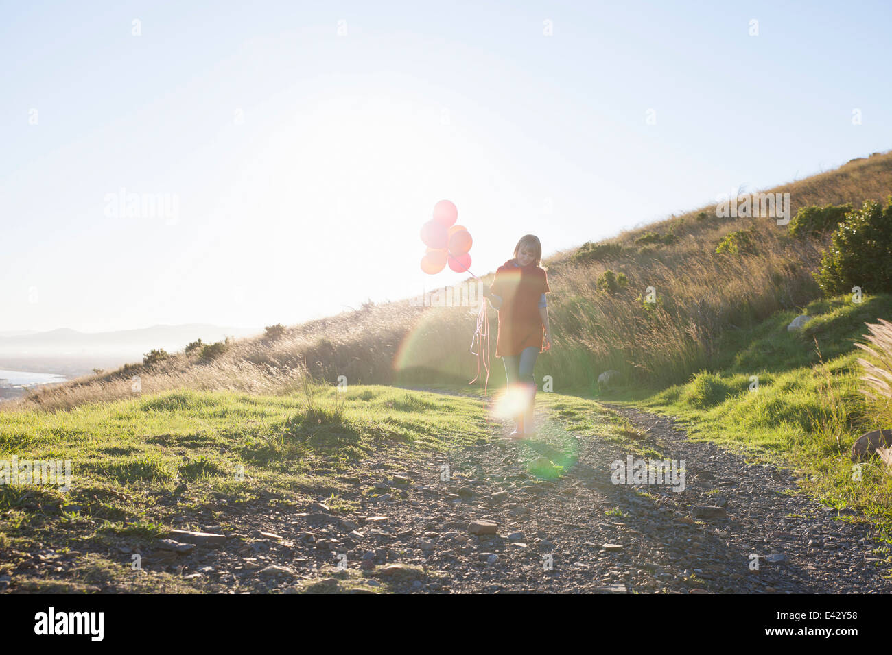 Young woman strolling along dirt track with bunch of balloons Stock Photo