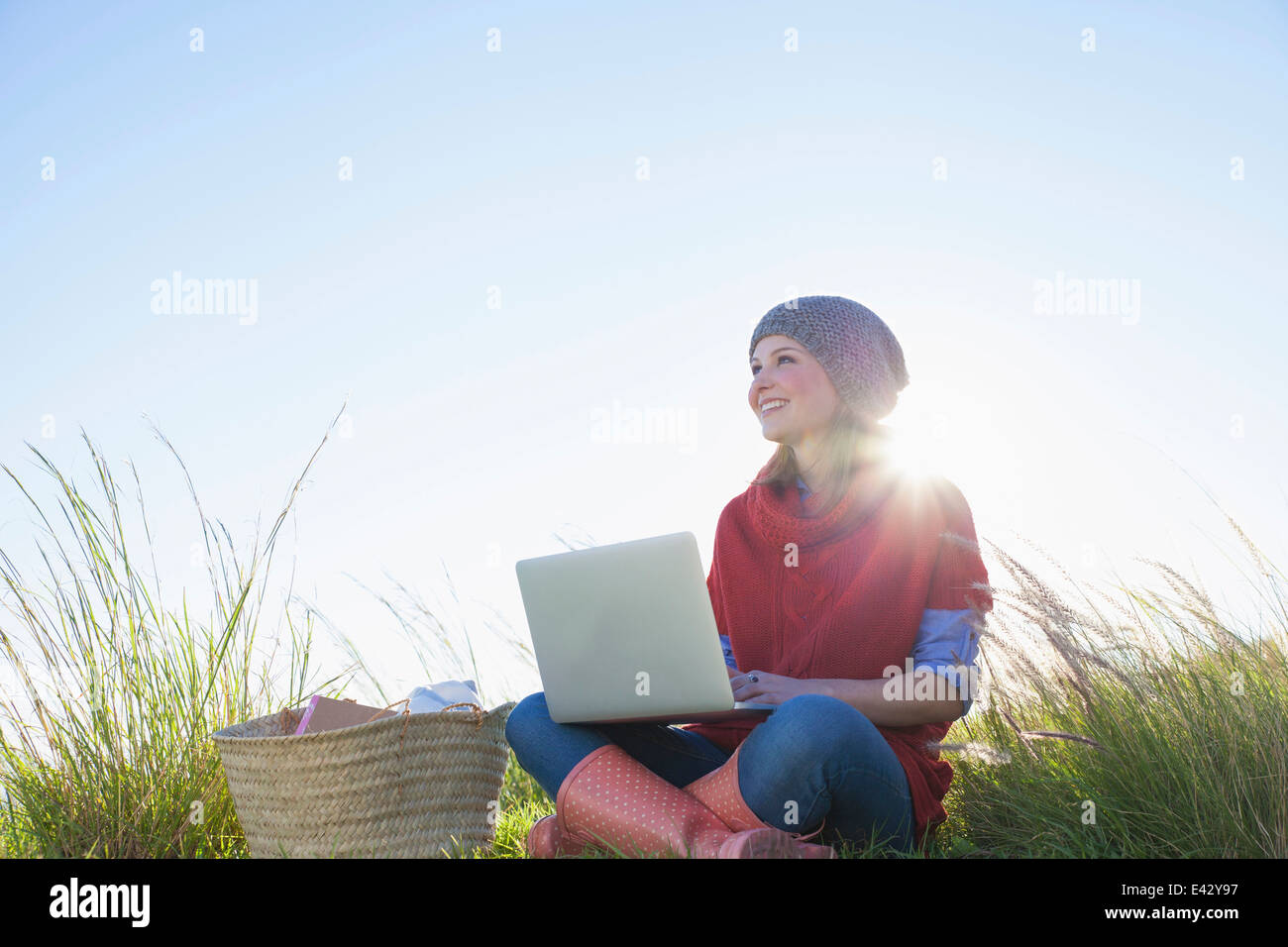 Young woman sitting in long grass using laptop Stock Photo