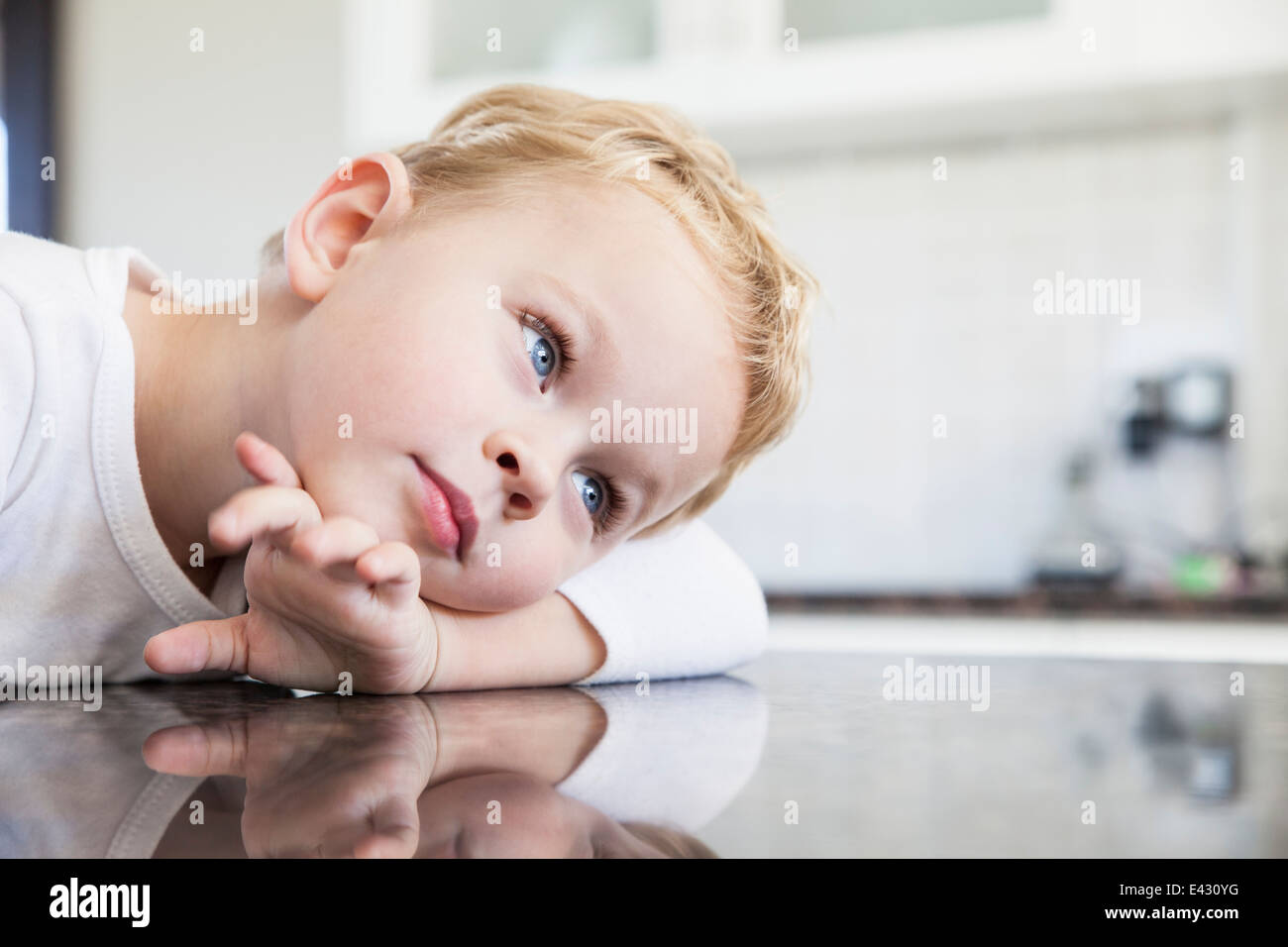 Portrait of three year old boy leaning on kitchen bench Stock Photo