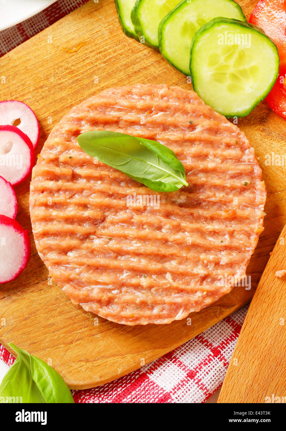 Raw burger patty and sliced vegetables on cutting board Stock Photo