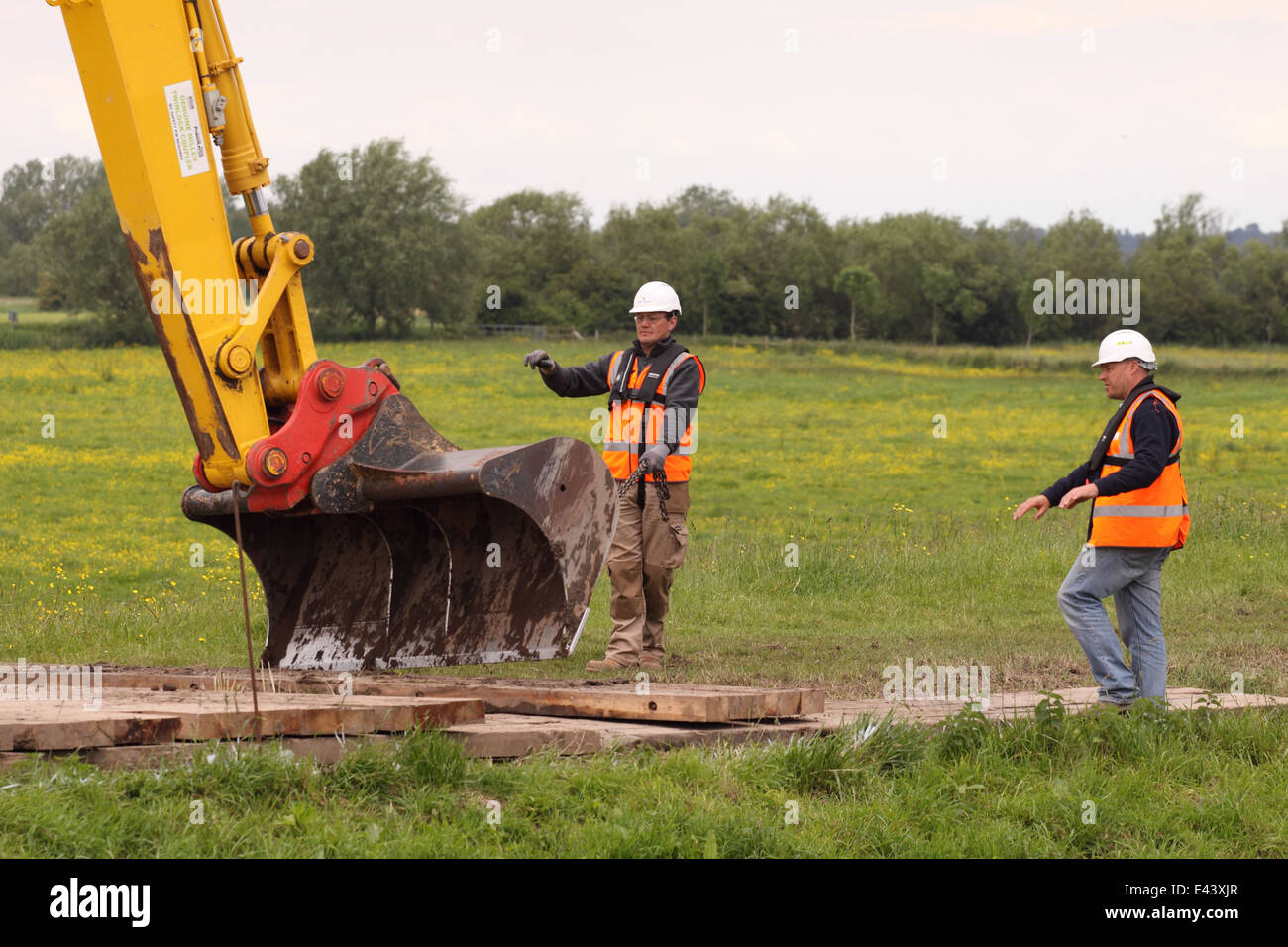 Environment Agency staff contractors working with an excavator digger wearing hard hats and high viz jackets Stock Photo
