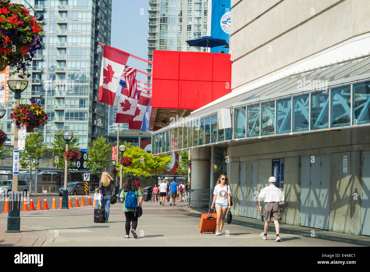 People walking in front of the Rogers Centre in downtown Toronto with the Canadian Flags flying on a summer day Stock Photo